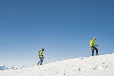 Seitenansicht von Wanderern, die auf einem schneebedeckten Berg gegen einen klaren blauen Himmel wandern - CAVF38534