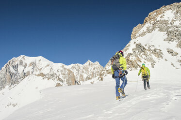 Rückansicht von Wanderern mit Rucksäcken klettern Berg gegen klaren blauen Himmel während sonnigen Tag - CAVF38535