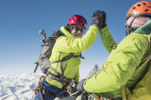 Wanderer geben sich beim Erklimmen eines Berges vor einem strahlend blauen Himmel die Hand - CAVF38539