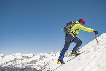 Side view of hiker climbing snow covered mountain against clear blue sky during sunny day - CAVF38553