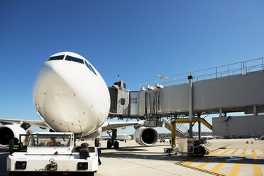 Airplane and passenger boarding bridge on runway against clear blue sky - CAVF38568