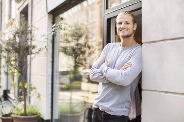 Portrait of smiling owner leaning on wall while standing outside clothing store - MASF04645