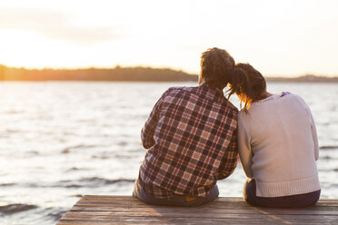 Rear view of loving couple sitting on pier against sea at sunset - MASF04648