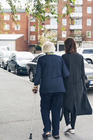 Rear view of elderly woman walking with granddaughter on sidewalk in city stock photo