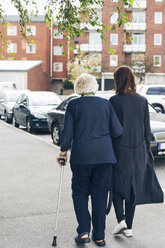 Rückansicht einer älteren Frau, die mit ihrer Enkelin auf dem Gehweg in der Stadt spazieren geht - MASF04657