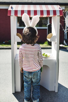 Rear view of boy standing at artificial concession stand on footpath - MASF04673