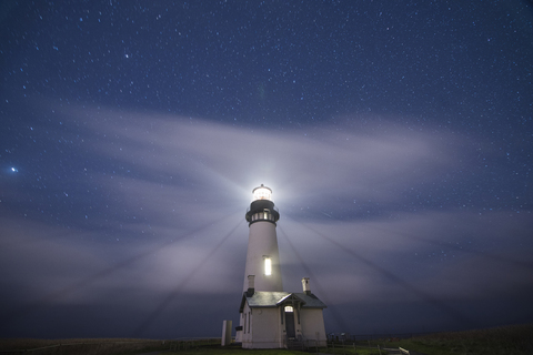 Low angle scenic view of Yaquina Head Lighthouse on shore against star field, lizenzfreies Stockfoto