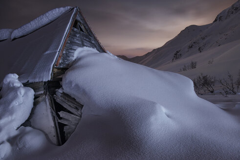 Snow covered log cabin against mountain at Independence Mine State Park - CAVF38706