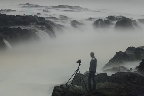 Digitales Kompositbild eines Wanderers, der den Thor's Well betrachtet, während er auf den Felsen steht - CAVF38741