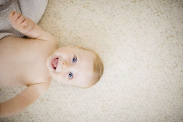 Overhead view of baby lying on rug at home laughing - CAVF38787