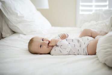 Cheerful baby boy lying on bed at home - CAVF38789