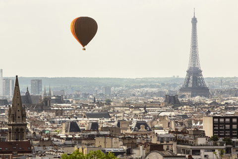 Heißluftballon fliegt über Stadtlandschaft mit Eiffelturm im Hintergrund, lizenzfreies Stockfoto