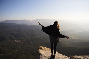 Rear view of woman gesturing while standing on cliff against mountains - CAVF38872