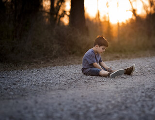 Boy playing with dirt on road during sunset - CAVF38900