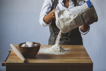 Midsection of woman removing flour from packet on table against wall - CAVF38957