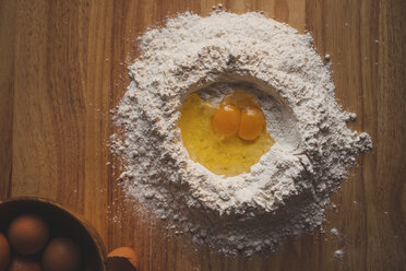 Overhead view of egg yolks and flour on wooden table - CAVF38960