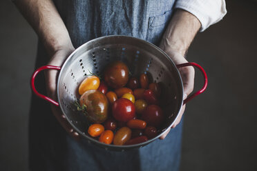 Midsection of man holding tomatoes in colander - CAVF38962