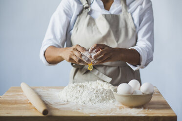 Midsection of woman breaking egg in flour on table while standing against wall at home - CAVF38967