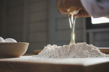 Cropped image of woman breaking egg in flour on table - CAVF38968