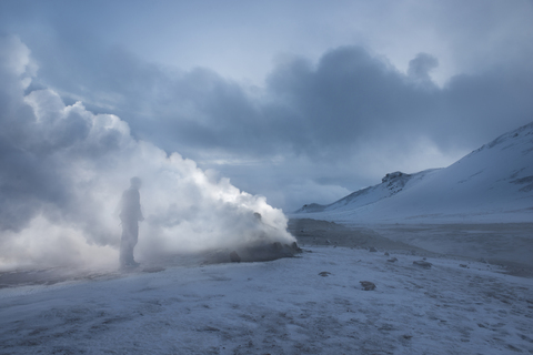 Mann steht neben Fumarolen, die auf einem schneebedeckten Feld Dampf ausstoßen, lizenzfreies Stockfoto