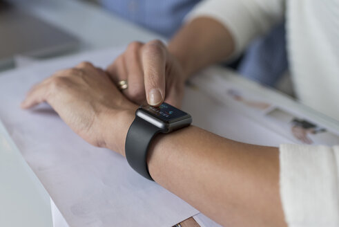 Frauenhand stellt Smartwatch am Schreibtisch ein - PAF01813
