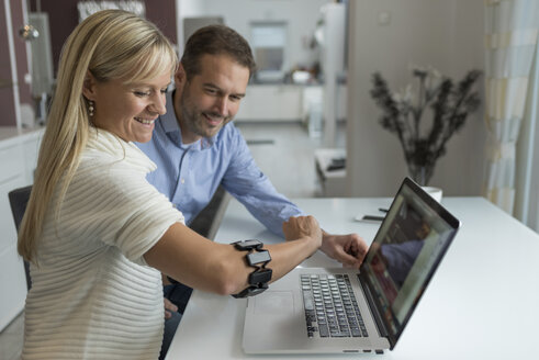Mann und lächelnde Frau mit Wearable an ihrem Arm am Schreibtisch - PAF01815