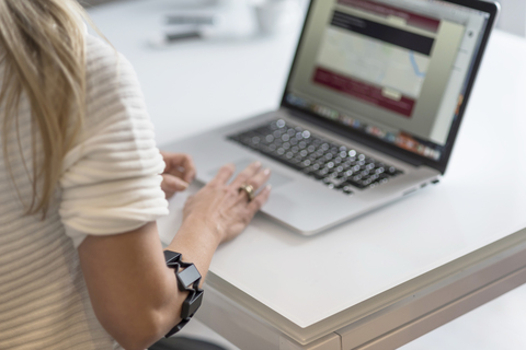 Frau mit Wearable am Arm benutzt Laptop am Schreibtisch, lizenzfreies Stockfoto