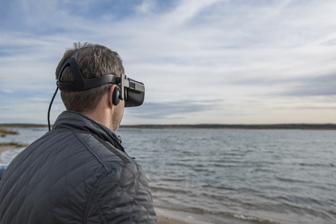 Mann mit VR-Brille am Seeufer, lizenzfreies Stockfoto
