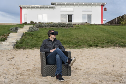 Mann sitzt im Sessel am Strand und trägt eine VR-Brille - PAF01826