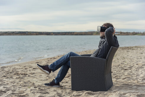 Mann sitzt im Sessel am Strand und trägt eine VR-Brille - PAF01827