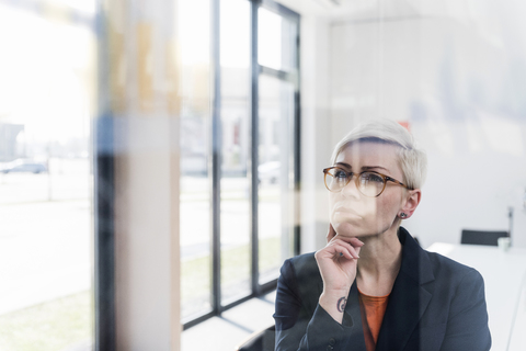 Konzentrierte Geschäftsfrau mit Blick auf eine Glasscheibe im Büro, lizenzfreies Stockfoto