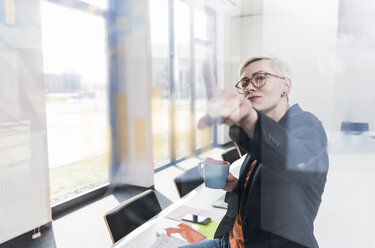 Confident businesswoman looking at glass pane in office - UUF13329