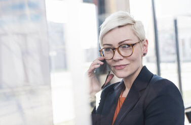 Porträt einer selbstbewussten Geschäftsfrau mit Handy im Büro - UUF13332