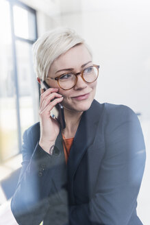 Porträt einer selbstbewussten Geschäftsfrau mit Handy im Büro - UUF13333