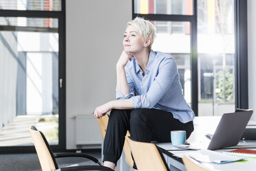 Lächelnde Frau sitzt auf einem Tisch im Büro - UUF13342