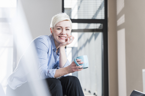 Porträt einer lächelnden Frau, die auf einem Tisch im Büro sitzt, lizenzfreies Stockfoto