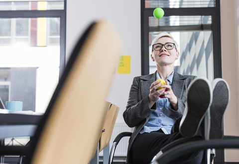 Lächelnde Geschäftsfrau, die im Büro mit Bällen jongliert, lizenzfreies Stockfoto