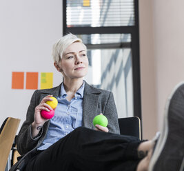 Businesswoman holding juggling balls in office - UUF13361