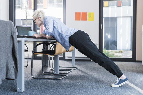 Businesswoman in office doing push ups on desk - UUF13364