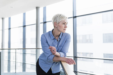 Woman in office building leaning on railing - UUF13365