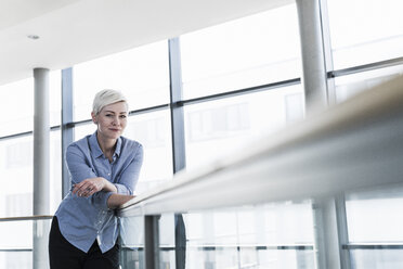 Portrait of woman in office building leaning on railing - UUF13366