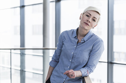 Porträt einer Frau in einem Bürogebäude, die sich auf ein Geländer stützt - UUF13367