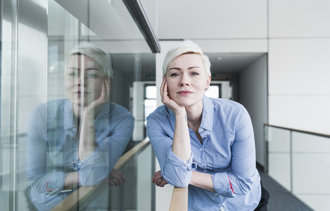 Porträt einer Frau im Büro, die sich auf ein Geländer stützt, lizenzfreies Stockfoto