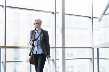 Businesswoman with takeaway cup standing in office building at glass front - UUF13373