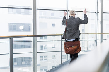 Frau auf Büroetage, die mit Kopfhörern Musik hört - UUF13376