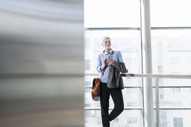 Smiling woman in office building using cell phone - UUF13378