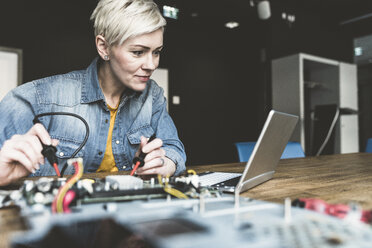 Frau arbeitet an einer Computerausrüstung und schaut auf einen Laptop - UUF13394