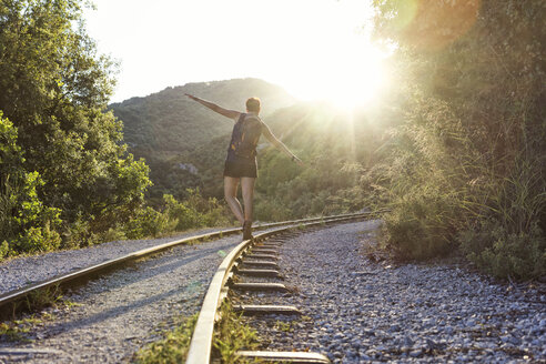 Griechenland, Pilion, Milies, Rückenansicht einer Frau, die bei Sonnenuntergang auf den Schienen der Schmalspurbahn balanciert - MAMF00053