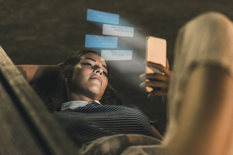 Young woman lying on bench at night with text emerging from smartphone stock photo