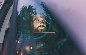 Fokussierter Mann im Auto bei Nacht, umgeben von einer Projektion auf das Armaturenbrett - UUF13403